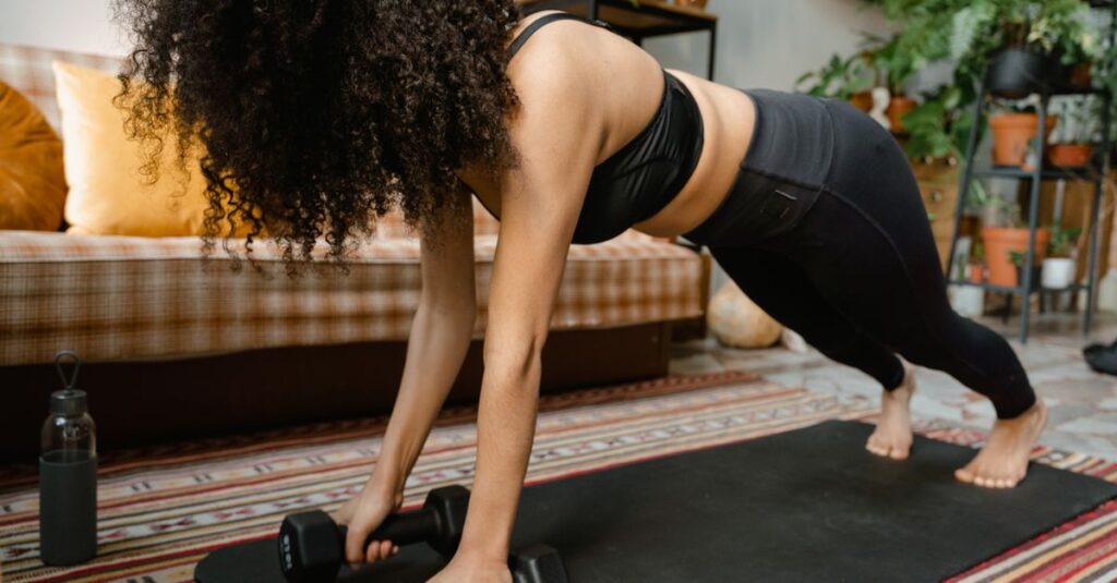 Woman performing push-ups with dumbbells on yoga mat in cozy indoor setting.
