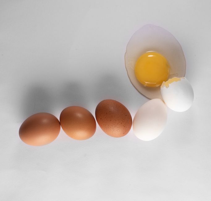 A collection of brown and white eggs next to a cracked egg on a clean white background.