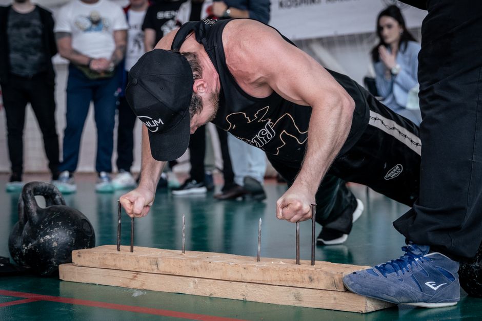 A man doing finger push-ups on nails during a gym competition with spectators watching.