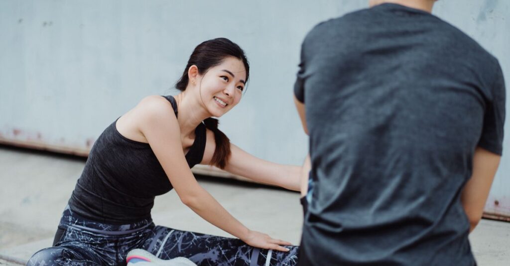 Young Asian woman smiling while stretching outdoors during a fitness session.