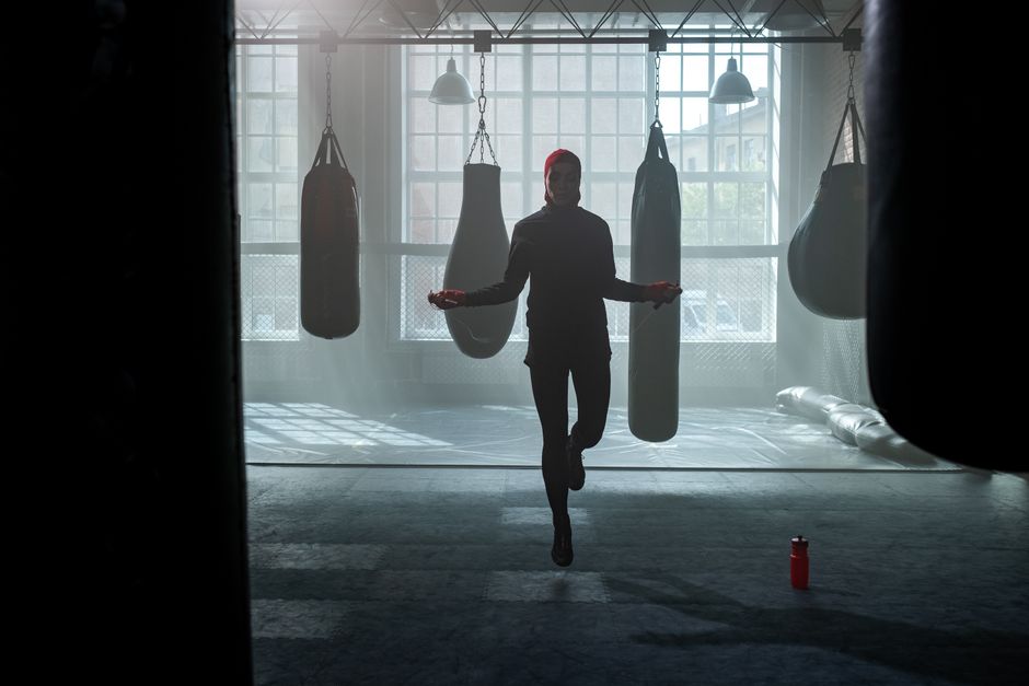 A woman exercises by jumping rope in a gym filled with punching bags.