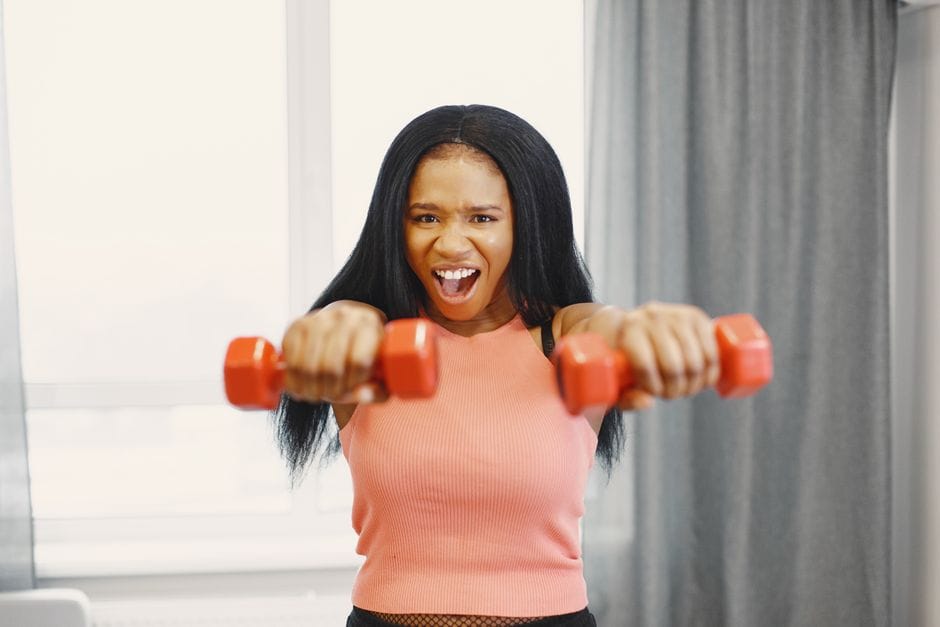 A cheerful woman lifts red dumbbells indoors, showcasing fitness and strength.