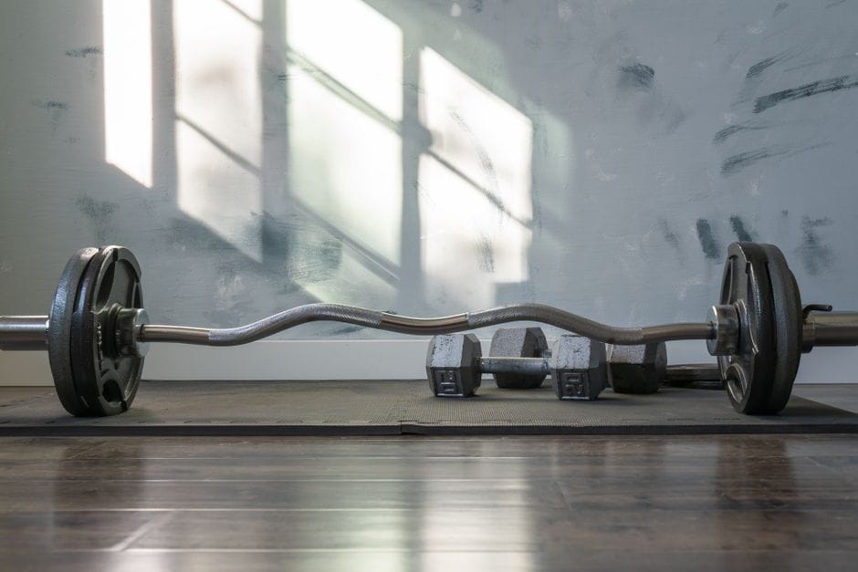 Barbell and dumbbells indoors on a gym mat with sunlight streaming through the window.