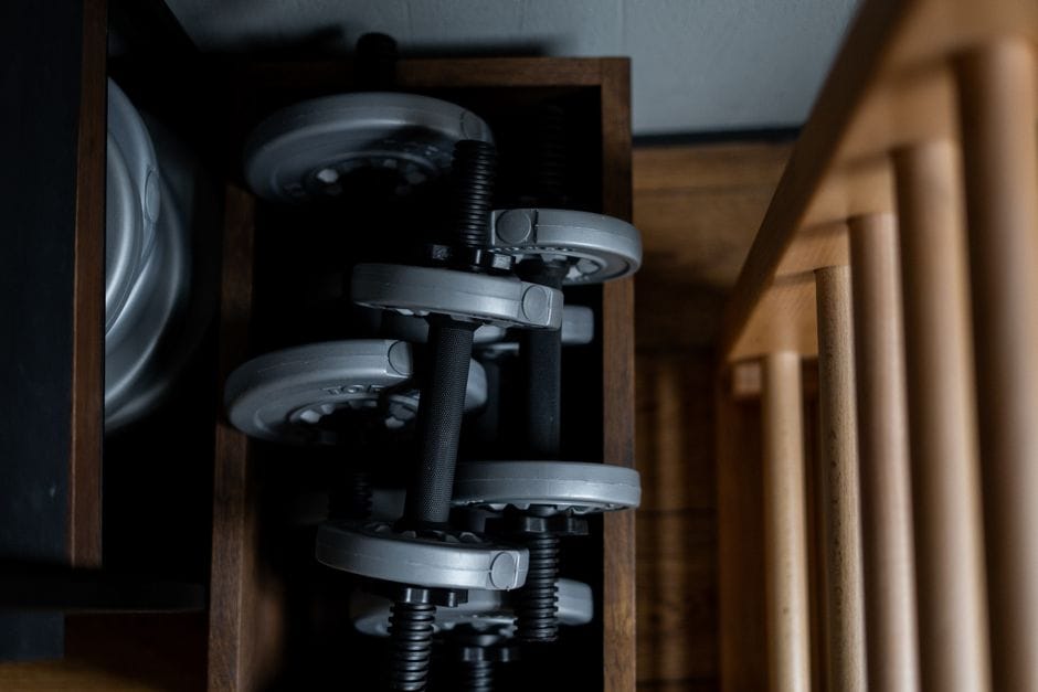 Home gym equipment organized in apartment corner with pegboard and shelves