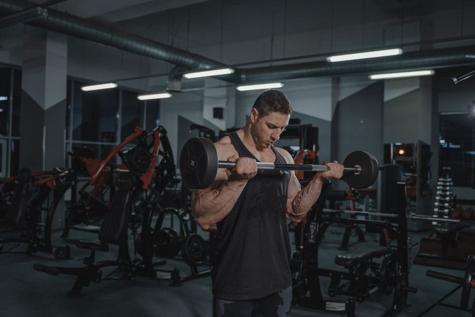 Muscular man intensely lifting a barbell in a well-equipped gym setting.