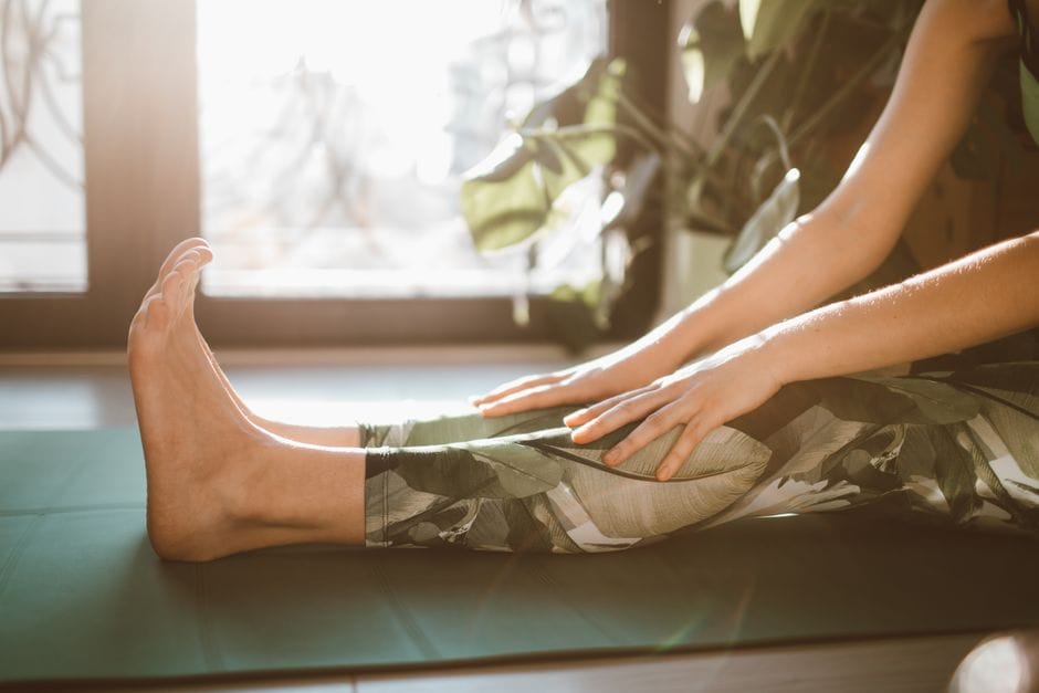 Person doing a gentle stretch for sore leg muscles on a yoga mat