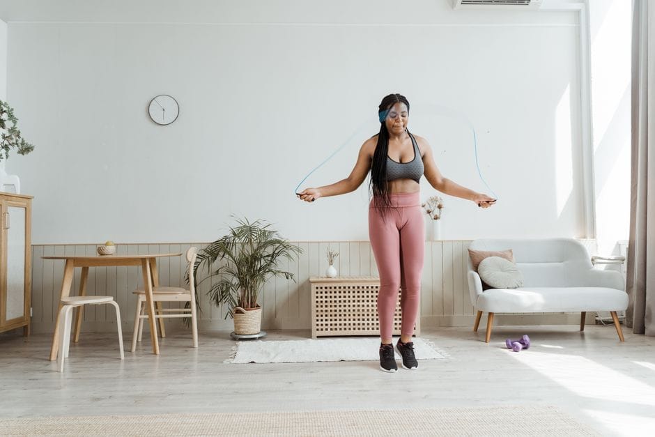 Confident black woman in activewear jump roping at home, promoting wellness and body positivity.