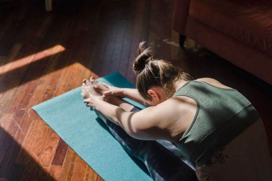 A woman stretches in a yoga pose on a mat in a sunlit room, emphasizing relaxation.