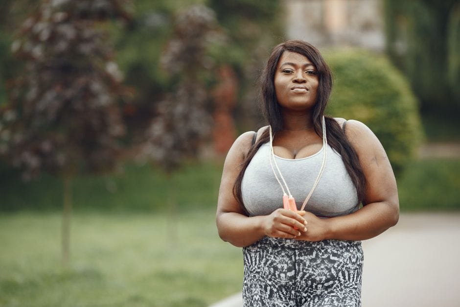 Plus size woman holding a jump rope, smiling confidently outdoors, embracing fitness lifestyle.
