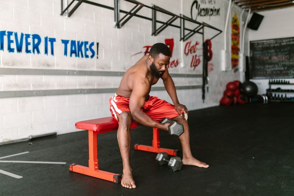 Man performing a Bulgarian split squat with his rear foot elevated on a bench, holding dumbbells at his sides