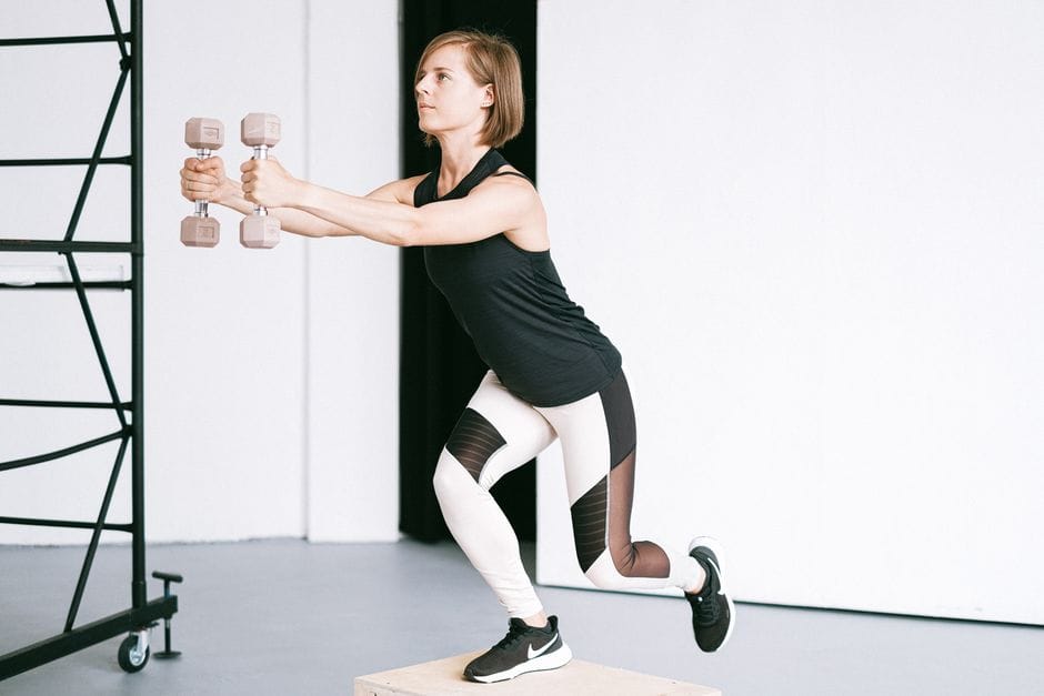 A woman in sportswear holds dumbbells while exercising indoors.