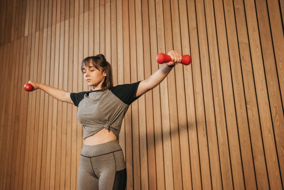 Person performing a dumbbell lateral raise with correct form, arms slightly bent, raising to shoulder height